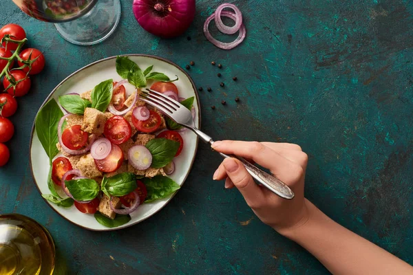 Abgeschnittene Ansicht einer Frau, die köstlichen italienischen Gemüsesalat Panzanella auf texturierter grüner Oberfläche mit Zutaten isst — Stockfoto