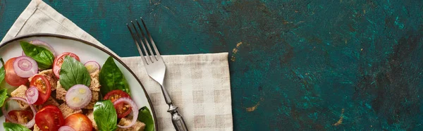 Vista superior de la deliciosa ensalada de verduras italiana panzanella servido en el plato en la superficie verde con textura con servilleta y tenedor, tiro panorámico - foto de stock