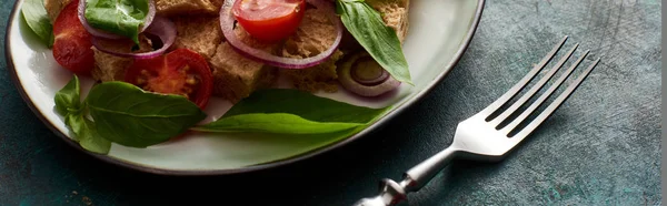 Vista de perto da deliciosa salada de legumes italiana panzanella servido na placa na superfície verde texturizada com garfo, tiro panorâmico — Fotografia de Stock