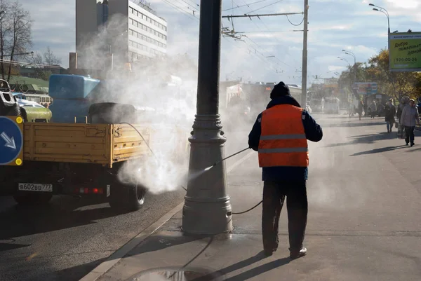 Octobre 2017, Moscou, Russie. Un travailleur vêtu d'un gilet orange comme du papier et de la saleté provenant des piliers en bordure de route — Photo