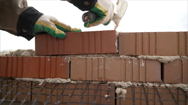 Worker in Close up of industrial bricklayer installing bricks and mortar cement brick on construction site. Worker builds a house of colored brick.