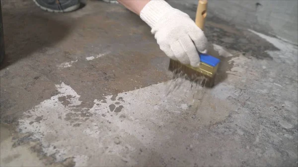 Stage of preparing the floor for waterproofing. A worker moistens a concrete floor with a brush. Wet concrete floor with a brush.