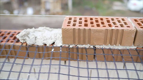 Worker builds a house of colored brick. Worker in Close up of industrial bricklayer installing bricks and mortar cement brick on construction site