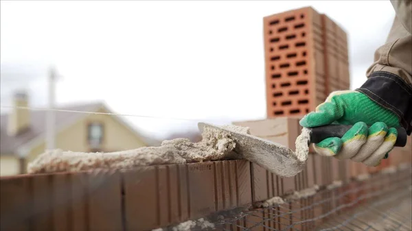 Bricklayer working in construction site of a brick wall. Bricklayer putting down another row of bricks in site. Worker puts a brick wall