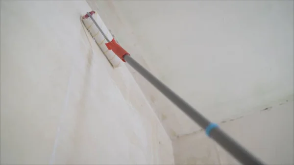 A man uses a roller to apply putty. Worker puts a wall with a roller. A man uses a roller to apply wallpaper glue to the wall.