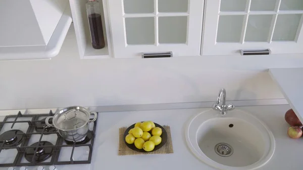 A plate with lemons is standing on the countertop. Bright white kitchen. Kitchen set. White kitchen set.