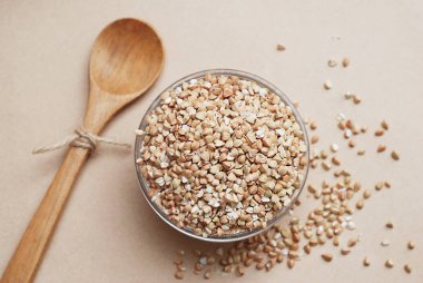 Üstten Görünüm ham yeşil buğday ve kahverengi Fildişi arka plan üzerinde cam kapta buğday kavrulmuş. Sağlıklı gıda ve beslenme kavramı. Düz yatıyordu. Tahta kaşık. Kopya alanı.