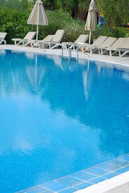 Sweeming havuz mavi su ile güneş şemsiyesi ve contloller. Dikey görüntü. Yaz ve tatil kavramı.