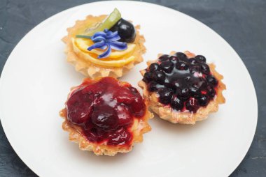 Ahududu koyu arka plan üzerinde beyaz tabakta ile üç Tartlets. Şekerli tatlı.