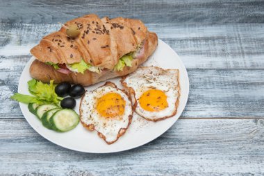 Bir tabak kızarmış yumurta sandviç kruvasan, salatalık, Siyah Zeytin rustik gri arka plan üzerinde. Üstten Görünüm. Sabah yemek. kopya alanı metin için.