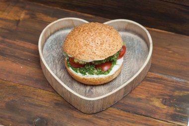 Kopyalama alanı rustik ahşap zemin üzerine taze sebze ile ahşap kalp şekli kutusunda, ev yapımı hamburger Üstten Görünüm.