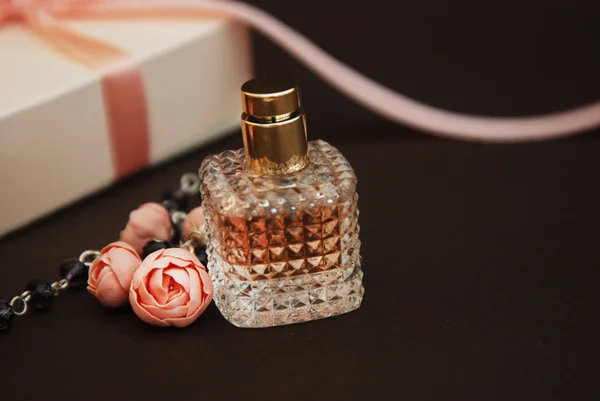 Frauen rosa Parfüm in schönen Flasche und künstliche Blumen Armband auf braunem Hintergrund mit Geschenkboxen auf dem Hintergrund. Kopierraum. — Stockfoto