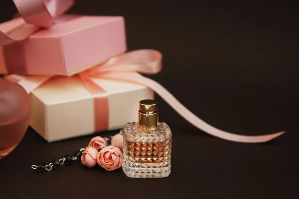 Frauen rosa Parfüm in schönen Flasche und künstliche Blumen Armband auf braunem Hintergrund mit Geschenkboxen auf dem Hintergrund. — Stockfoto