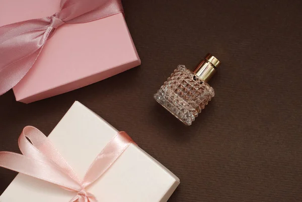 Frauen rosa Parfüm in schönen Flasche und künstliche Blumen Armband auf braunem Hintergrund mit Geschenkboxen auf dem Hintergrund. Wohnung lag mit Kopierraum. — Stockfoto