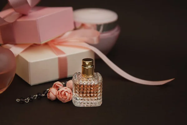Frauen rosa Parfüm in schönen Flasche und künstliche Blumen Armband auf braunem Hintergrund mit Geschenkboxen auf dem Hintergrund. — Stockfoto