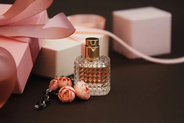 Frauen rosa Parfüm in schönen Flasche und künstliche Blumen Armband auf braunem Hintergrund mit Geschenkboxen auf dem Hintergrund. — Stockfoto