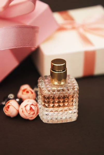 Frauen rosa Parfüm in schönen Flasche und künstliche Blumen Armband auf braunem Hintergrund mit Geschenkboxen auf dem Hintergrund. — Stockfoto