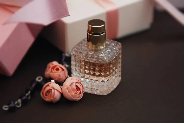 Frauen rosa Parfüm in schönen Flasche und künstliche Blumen Armband auf braunem Hintergrund mit Geschenkboxen auf dem Hintergrund. — Stockfoto