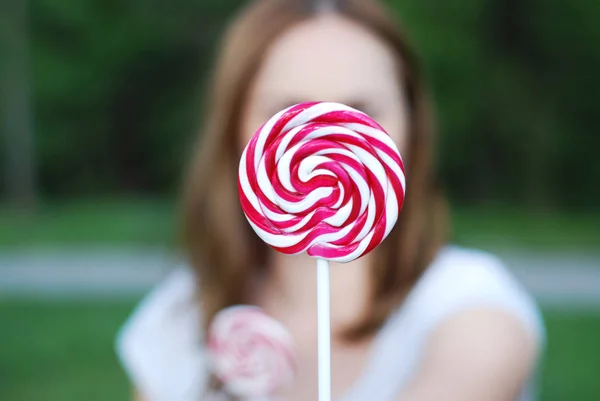 Close Up Swirl Lolipop Holding by a Blured Lovely Young Woman, Blured Green Garden Background. — Stock Photo, Image