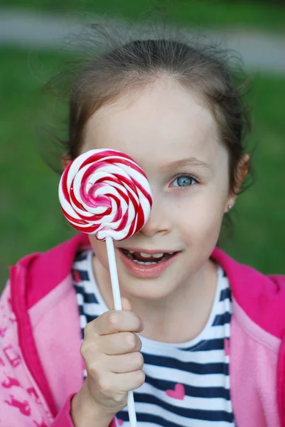 Adorable little Caucasian Girl Holding Lollipop or Sweet Candy Happy Expressions. Standing over Blured Green Grass Background — Stock Photo, Image
