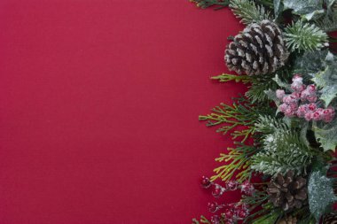 Noel kırmızı arka planı, köknar dalları, çam kozalakları, beyaz arka planda çelenk. Kopyalama alanı olan üst görünüm.