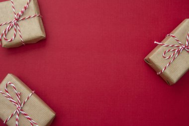 Kırmızı arka planda el işi hediye kutuları. Fotokopi alanı olan bir Noel modeli. Kış tatillerinde hediyeler, üst manzara, düz yatak.