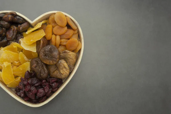 Mezcla de frutas secas, en caja de madera en forma de corazón aislada sobre fondo oscuro. Vista superior de varios higos de frutos secos, albaricoques, mango, arándanos . — Foto de Stock