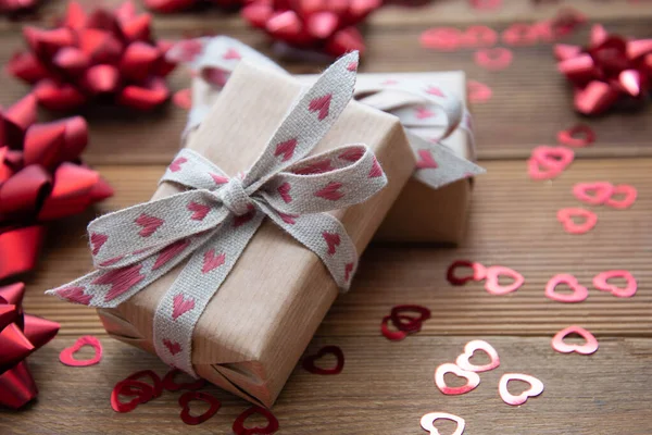 Kraft barna papír ajándék doboz piros íjak és konfetti, fa alapon. Valentin-nap, Születésnap, Party koncepció. — Stock Fotó