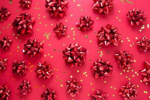 Κόκκινα τόξα και χρυσή λάμψη σε σχήμα καρδιάς, πάνω από το κόκκινο φόντο, επίπεδη lay. Πάρτι, γενέθλια, Χριστούγεννα ή του Αγίου Βαλεντίνου μοτίβο. Επίπεδη. — Φωτογραφία Αρχείου