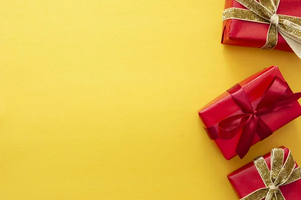 Horní pohled na červené dárkové krabice s stuhou přes barevné žluté pozadí. Valentýn, vánoční nebo narozeninový koncept. — Stock fotografie