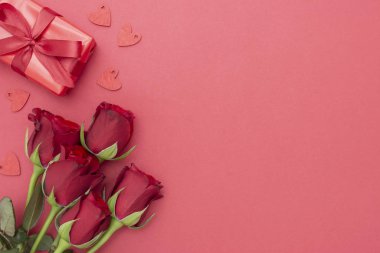 Sevgililer Günü, kırmızı güller ve kurdeleli hediye kutusu, kırmızı arka planda düz bir zemin, fotokopi alanı olan soyut doğum günü arkaplanı..