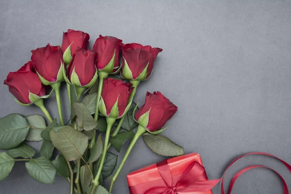 Día de San Valentín, rosas rojas y caja de regalo con cinta, sobre fondo gris plano, fondo abstracto de cumpleaños con espacio para copiar . — Foto de Stock