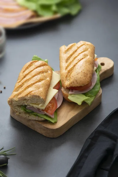 Sandwich con pane baguette, prosciutto, lattuga, pomodoro su fondo scuro. Colazione o fast food . — Foto Stock