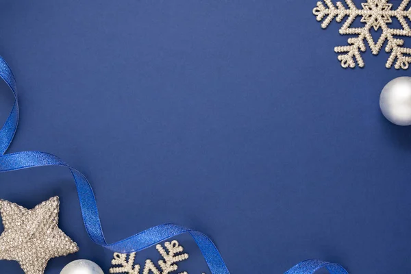 Mavi soyut Noel arkaplanı, gümüş kar taneleri, takılar ve mavi kurdeleli. Mavi metin için boşluk oluşturur.