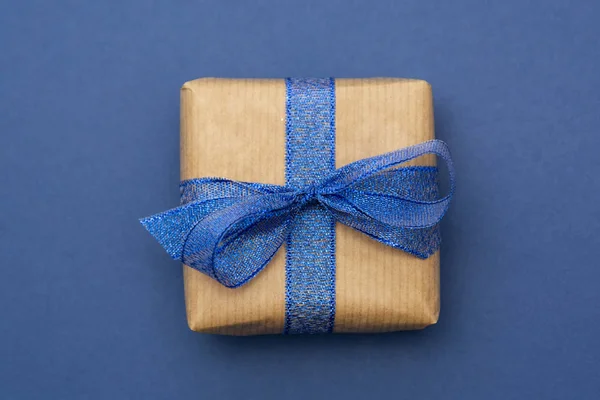 Craft paper wrapped gift box isolated on blue background, flat lay. Abstract Christmas gift.