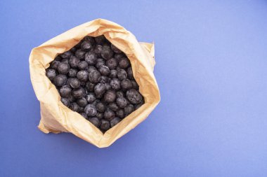 Yabanmersini arka planı. Mavi arka planda, kağıt torba içinde olgun ve sulu yabanmersini. Boşluğu kopyala.