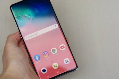 Corby, Birleşik Krallık. 25 Aralık 2019 Samsung Galaxy S10 cep telefonu, mavi arka planda beyaz S10 ile el ele tutuşuyor. İllüstrasyon Editörü