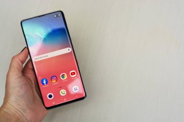 Corby, Birleşik Krallık. 25 Aralık 2019 Samsung Galaxy S10 cep telefonu, mavi arka planda beyaz S10 ile el ele tutuşuyor. İllüstrasyon Editörü
