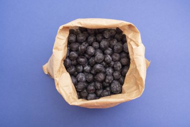 Yabanmersini arka planı. Mavi arka planda, kağıt torba içinde olgun ve sulu yabanmersini. Boşluğu kopyala.