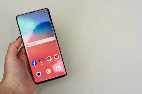 Corby, Birleşik Krallık. 25 Aralık 2019 Samsung Galaxy S10 cep telefonu, mavi arka planda beyaz S10 ile el ele tutuşuyor. İllüstrasyon Editörü