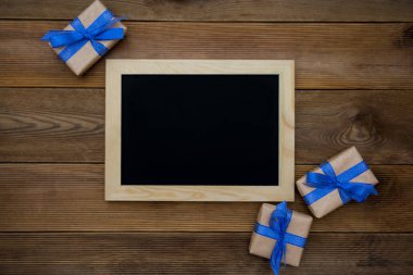 Mavi kurdeleli hediye kutuları ve ahşap masada boş karatahta. Üst görünüm.