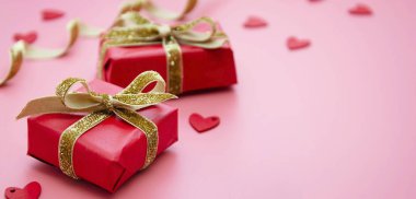 Kırmızı hediye kutusu ve altın fiyonk, pembe arka planda. Sevgililer Günü, Doğum günü, Parti konsepti.