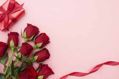 Sevgililer Günü, kırmızı güller ve kurdeleli hediye kutusu, kırmızı arka planda düz bir zemin, fotokopi alanı olan soyut doğum günü arkaplanı..