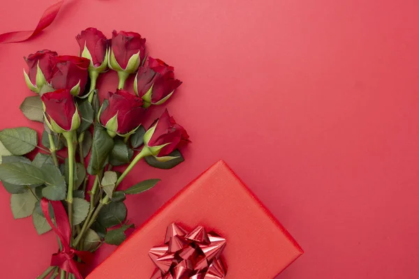 Rosas rojas y caja de regalo con cinta, sobre fondo rojo plano laico. Día de San Valentín, Fondo abstracto de cumpleaños con espacio para copiar . — Foto de Stock