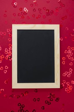 Kırmızı arkaplanda parlak konfeti olan boş karatahtanın üst görünümü.