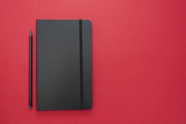Kırmızı arka planda siyah defter. Çalışma masasının üst görüntüsü, çalışma alanı. Soyut iş dairesi yatıyordu.