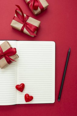 Sevgililer Günü modeli. Kırmızı kalpler ve hediye kutularının olduğu defteri kırmızı arkaplanda aç, metin için boşluğu kopyala.