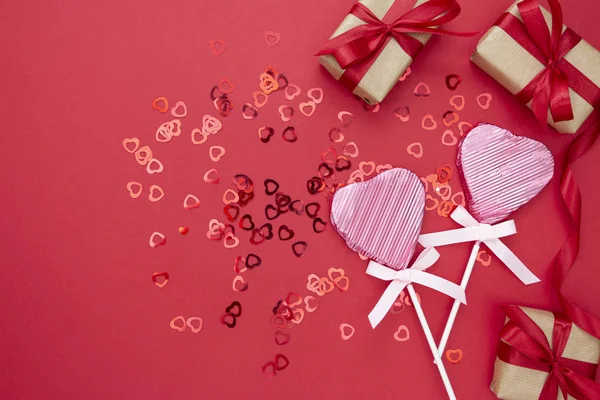 Love, Valentine 's Day mock up, with lollipop in the shape of a heart, gift boxex and glitter isolated on red background, copy space . — стоковое фото