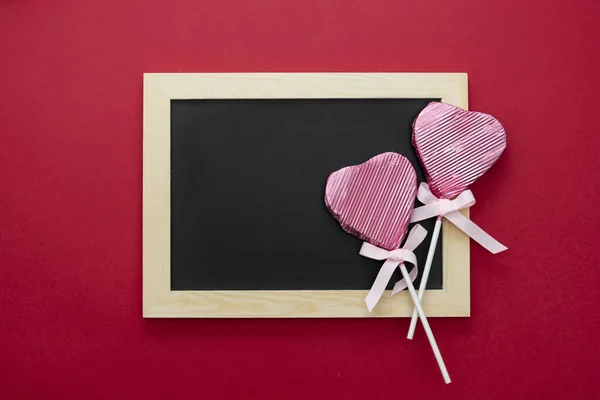 San Valentín maqueta, pizarra vacía con piruleta en forma de corazón y brillo aislado sobre fondo rojo, espacio de copia . — Foto de Stock