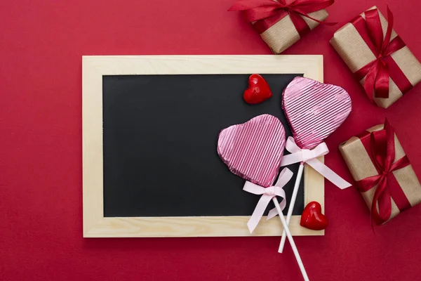 Valentin napi gúnyolódás, tábla nyalóka alakú szív, ajándék dobozok és csillogás elszigetelt piros háttér, másolás helyet. — Stock Fotó